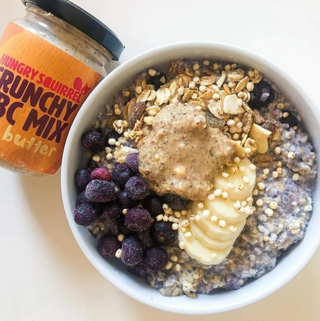  bowl of granola with berries and banana next to a jar of crunchy ABC mix nut butter