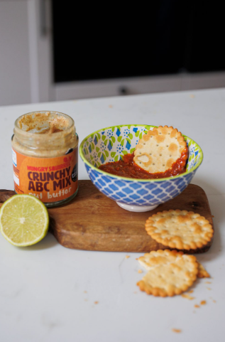 Jar of crunchy ABC mix nut butter, bowl with crackers and dip, lime, and crackers on a white surface.