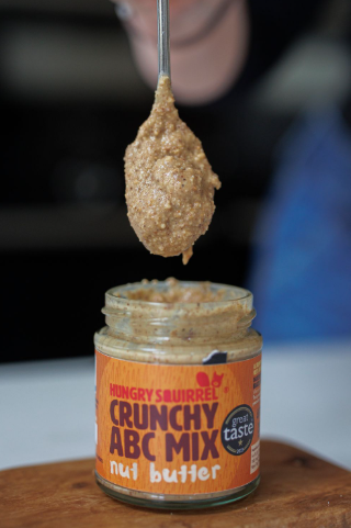 Jar of crunchy ABC mix nut butter with a spoonful above it on a wooden surface.