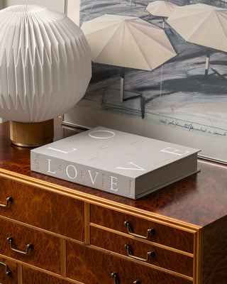 Book titled 'All You Need is LOVE' on a wooden dresser with decorative items and a painting in the background.