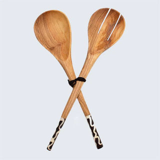 Two crossed wooden salad server spoons with decorative black and white handles on a light gray background