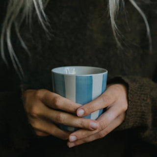 Person holding a blue and white striped mug with a dark background
