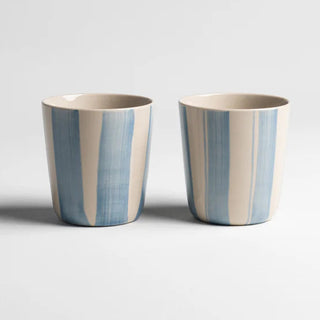 Two ceramic cups with blue and beige stripes on a light gray background