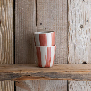 Two ceramic cups with red and white stripes stacked on a wooden surface with a wooden panel background.
