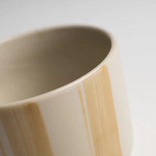 Close-up of a ceramic mug with beige and brown stripes on a light gray background