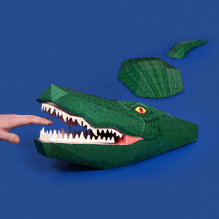 3d paper green crocodile with hand near teeth against a blue background