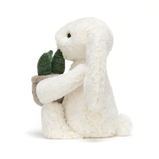 Side facing white plush bunny holding a small potted plant on a white background