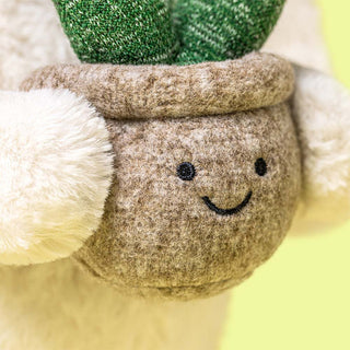 Close-up of a plush toy holding a smiling beige plant pot with green plant