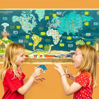 2 young girls playing with dinosaur cut outs infront of the Dinosaur Timeline & World Map against an orange wall