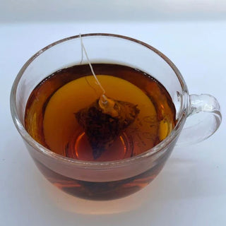 Clear glass mug with tea being brewed, showing a tea bag in the liquid.