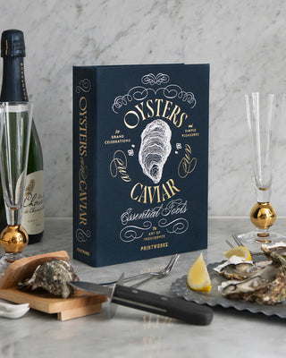 Navy blue Oysters & Caviar display box on a kitchen worktop surrounded by oysters, lemons, champagne and flutes.