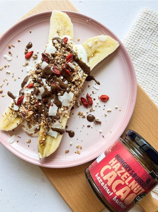 Bananas with toppings on a pink plate next to a jar of Hazelnut Cacao nut butter.