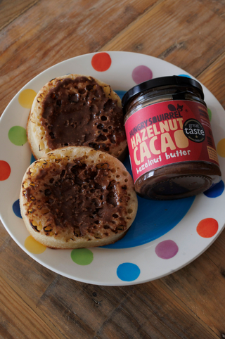 Two crumpets spread with hazelnut cacao nut butter on a polka dot plate.