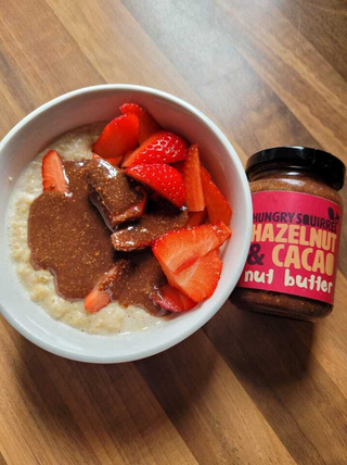 Porridge bowl with strawberries and a jar of hazelnut and cacao spread on a wooden surface