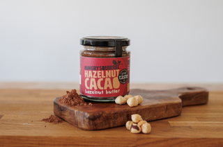 Jar of hazelnut cacao nut butter on a wooden cutting board with hazelnuts