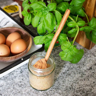 Jar of spices with a heart shaped wooden spoon, eggs, and basil leaves on a kitchen counter.