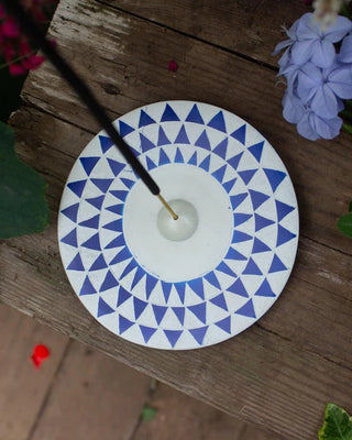 Round incense holder with blue triangle pattern on a wooden surface with flowers.