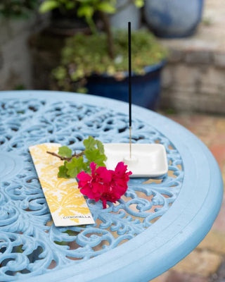 Incense stick with white & yellow floral decoration packaging on a blue table outdoors