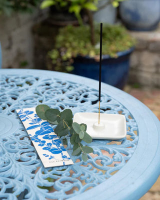 Incense stick on a white dish with green leaves and a blue and white packaging on a decorative table.