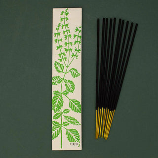 Incense sticks with a green leaf design on a beige card against a dark green background