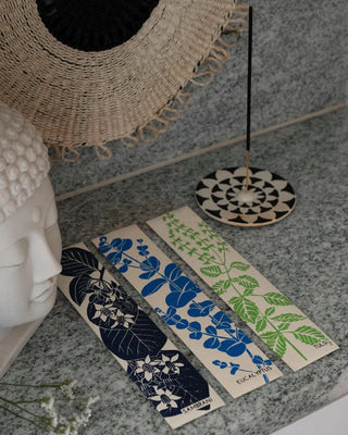 Decorative packaging with floral designs on a stone surface next to a woven basket and a Buddha statue.