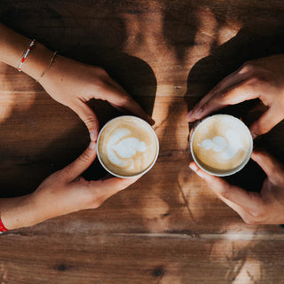 Hands holding cups of cappuccino on a wooden table