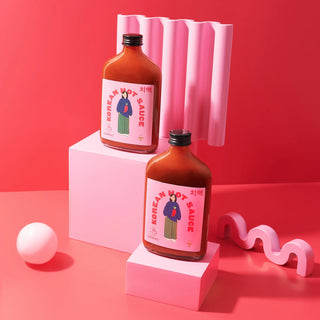 Two glass bottles of Korean Hot Sauce with pink labels and red text on top of geometric shapes against a hot pink background