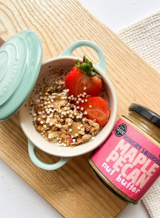 Overnight oats, nuts and strawberries in a ceramic dish next to a jar of maple pecan nut butter on a wood board