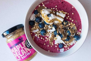 Smoothie bowl with toppings and a jar of maple pecan nut butter on a white background