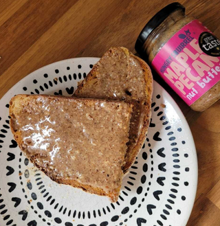 Two slices of toast with maple pecan butter on a plate, next to a jar of the same butter.