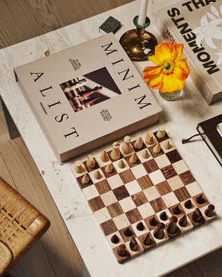 Wooden chessboard with pieces on a table next to its display box titled 'Minimalist'.