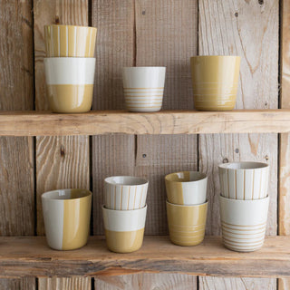 Set of ceramic cups with two-tone yellow & white design on wooden shelves against a rustic wooden wall.