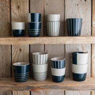 Set of ceramic cups with dark green and white design on wooden shelves.