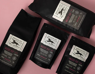 Four pouch bags of Mucky Pup coffee lying down against a pink background