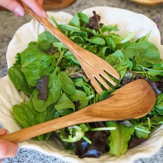 Wooden salad servers in a bowl of green salad leaves