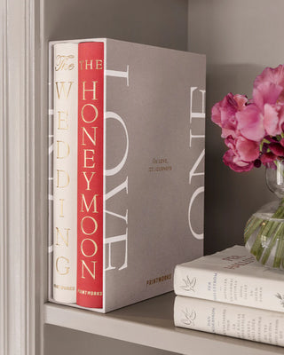 Decorative books titled 'The Wedding' and 'Honeymoon' in a display case titled 'Love' on a shelf with a vase of pink flowers.