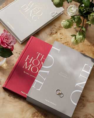 Two books titled 'The Wedding' and 'The Honeymoon' in a display case titled 'Love' on a wooden surface with flowers.