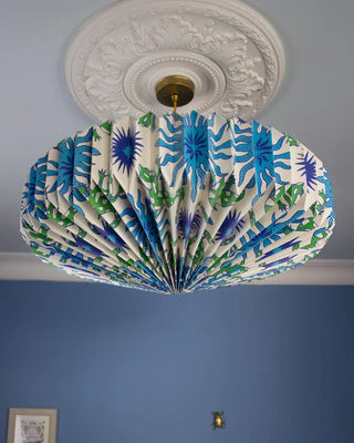 Ceiling light fixture with decorative origami paper fan with blue & green pattern against a blue wall.