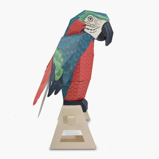 side view of a 3d paper parrot on a perch against a white background