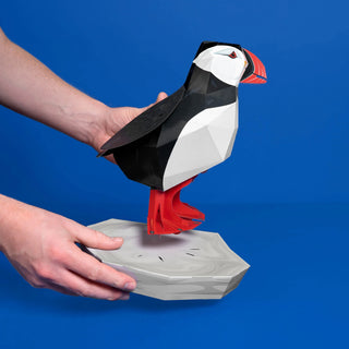 3D paper model of a puffin held by a person against a blue background