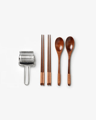 Set of wooden chopsticks and spoons with a metal pasta cutter tool on a white background