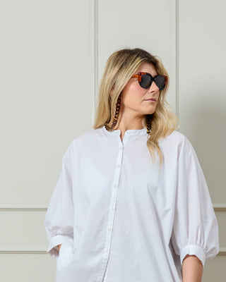 Woman wearing a white shirt and sunglasses with a tortoiseshell glasses chain against a neutral background
