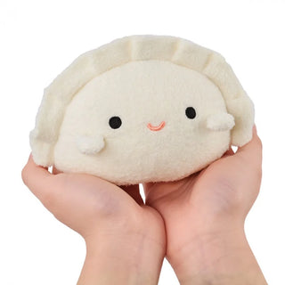 Plush toy resembling a dumpling held in hands against a white background