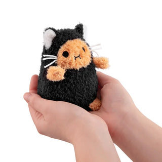 Small plush toy resembling a black cat with orange face held in hands against a white background