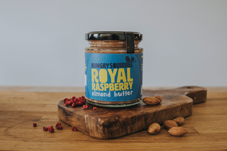 Jar of Hungry Squirrel Royal Raspberry Almond Butter on a wooden cutting board with almonds and raspberries.