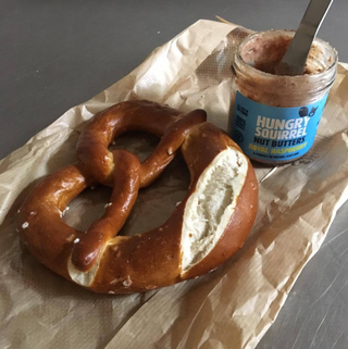 Pretzel with a jar of 'Hungry Squirrel Nut Butter' on brown paper