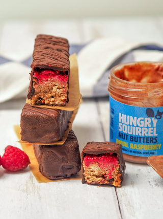 Chocolate-covered snack bar with raspberry filling next to a jar of 'Hungry Squirrel' Royal Raspberry nut butter.