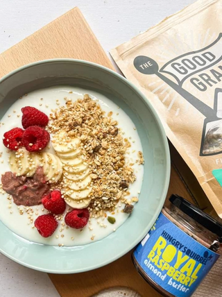 Yogurt bowl with granola, bananas, and raspberries next to a bag of Granola and a jar of Royal Raspberry Almond Butter