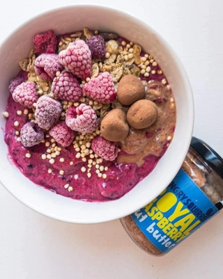 Acai bowl with raspberries, granola, and a jar of Royal Raspberry Almond Butter on a white background