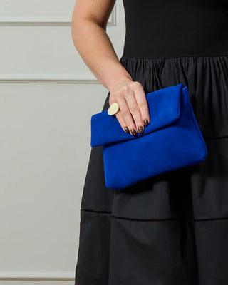 Person holding a blue clutch and wearing a cream chunky ring against a neutral background